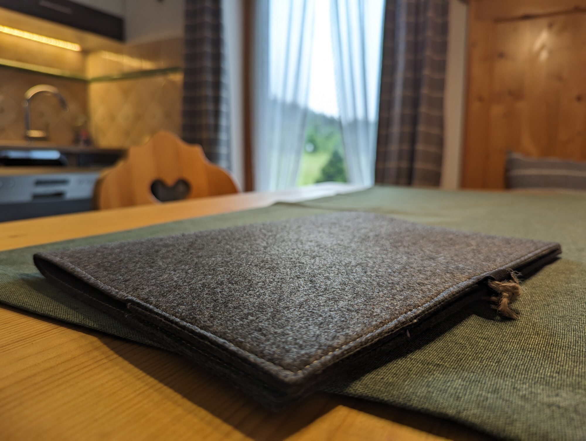 Detailaufnahme eines Filzordners auf einem Holztisch im Ferienhaus Wiesenhof in Klais, mit Blick auf die Küche im Hintergrund.