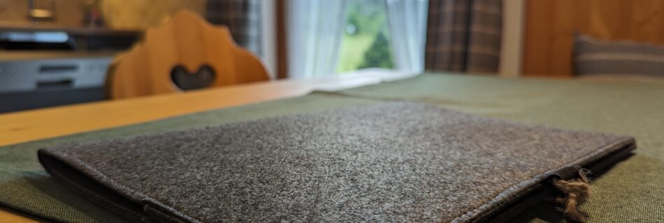 Detailaufnahme eines Filzordners auf einem Holztisch im Ferienhaus Wiesenhof in Klais, mit Blick auf die Küche im Hintergrund.