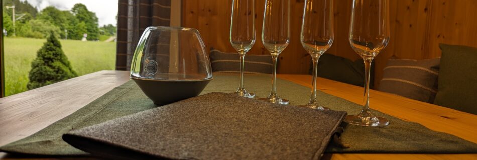 Gedeckter Tisch mit Champagnergläsern und Filzordner im Ferienhaus Wiesenhof in Klais. Große Fenster bieten einen Ausblick auf die umliegende Natur.