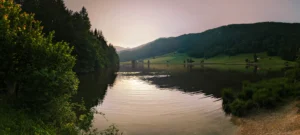 Sonnenuntergang über dem Geroldsee mit ruhigem Wasser, umrahmt von Wiesen, Bäumen und sanften Hügeln.