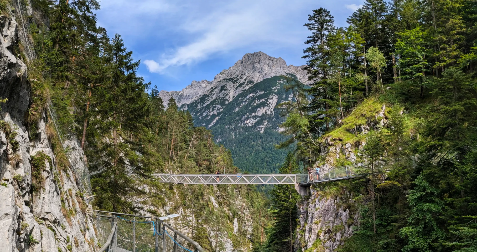 Metallgitterbrücke über eine enge Schlucht mit Blick auf das Karwendelgebirge