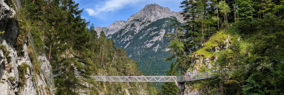 Metallgitterbrücke über eine enge Schlucht mit Blick auf das Karwendelgebirge