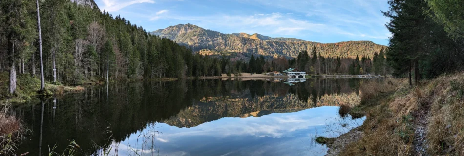 Panorama des Pflegersees im Herbst, umgeben von Wäldern und Felswänden.