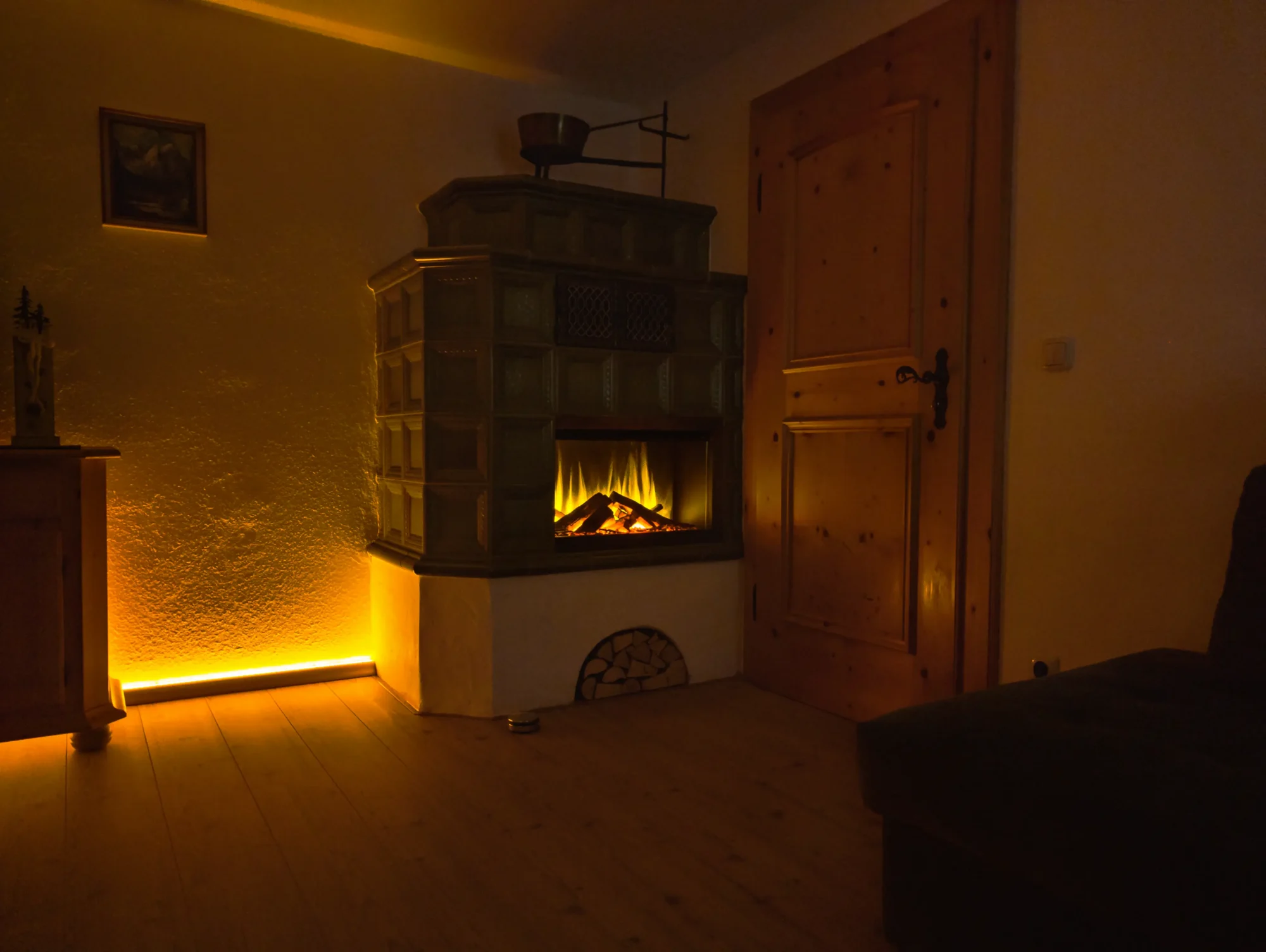 Wohnzimmer im Ferienhaus Wiesenhof mit traditionellem Kachelofen und integriertem Elektrokamin – stimmungsvolle Beleuchtung und warme Atmosphäre.